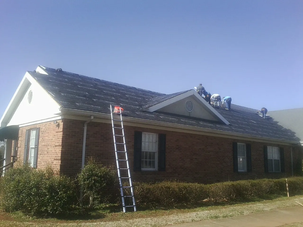 Crew tearing shingles off a brick ranch roof with a ladder set — Emergency Roof Repair work by our crew in Sunnyvale
