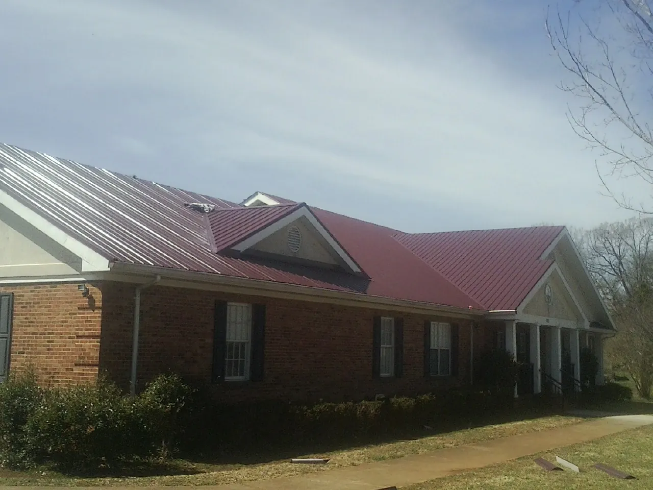 Red metal roof with gabled entries on a long brick building, from a Hail Damage Roof Repair job in Sunnyvale