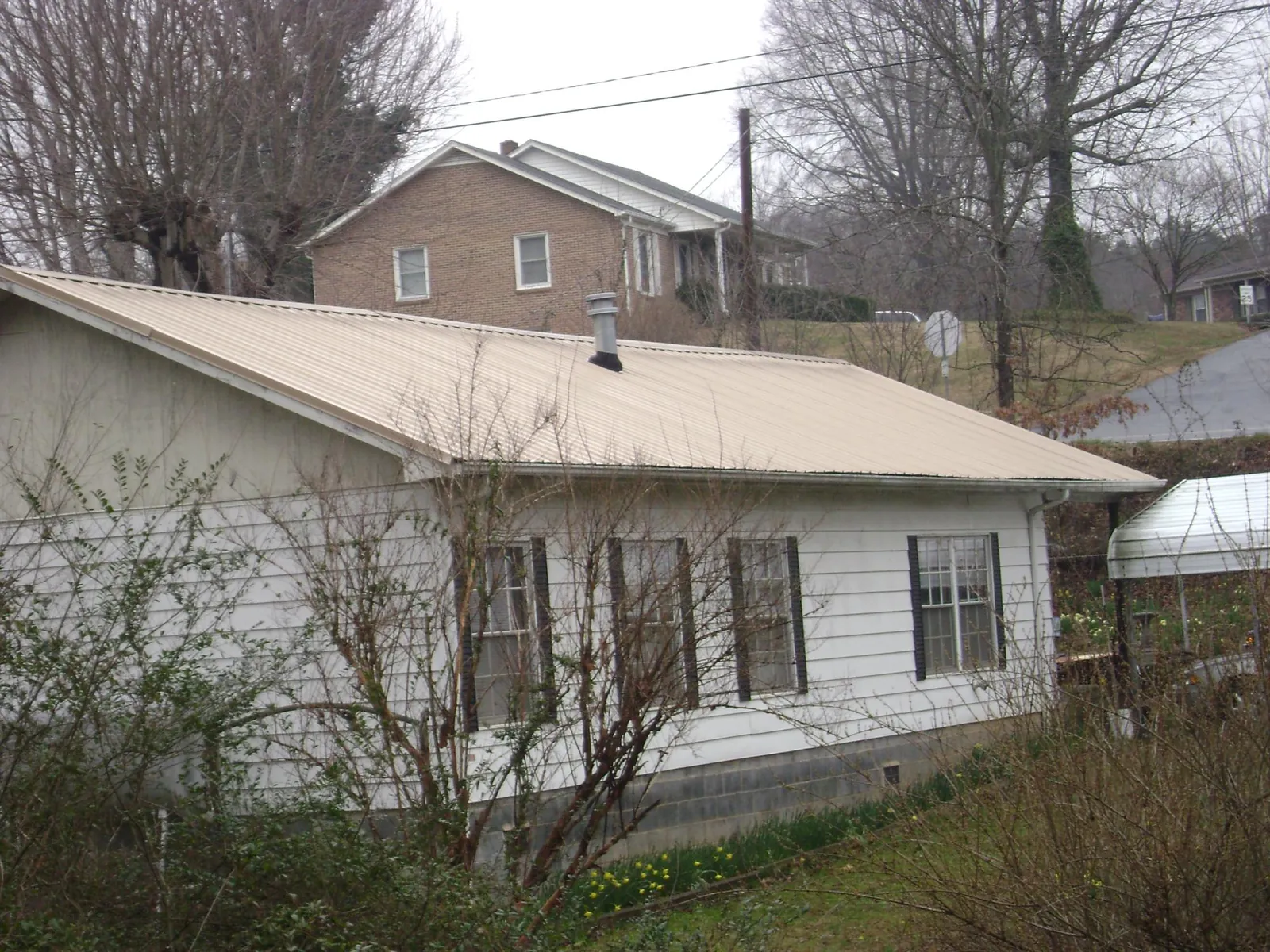 Tan metal roof on a white sided house set into a hillside — Commercial Roofing by Roofing Brothers in Sunnyvale